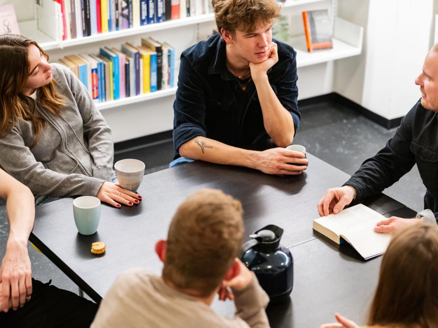 Gruppe omkring et bord, mand med bog. Foto: Christopher Egeberg (Flip)